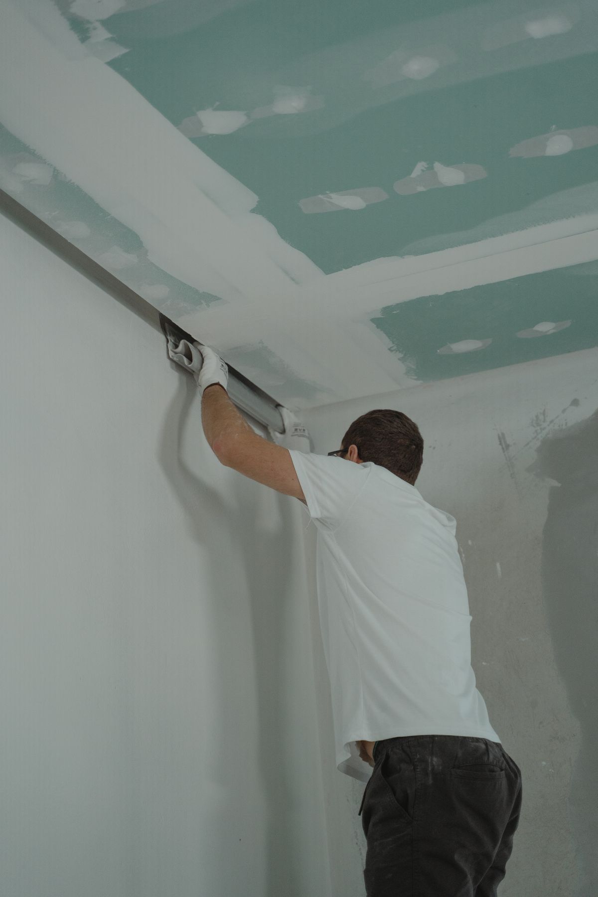 Finisher drawing a wide skimming blade along the joint where a ceiling meets the wall