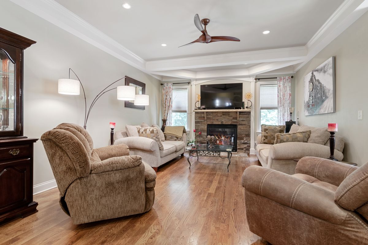 Living room with a smooth white ceiling, crown molding, ceiling fan, and stone fireplace