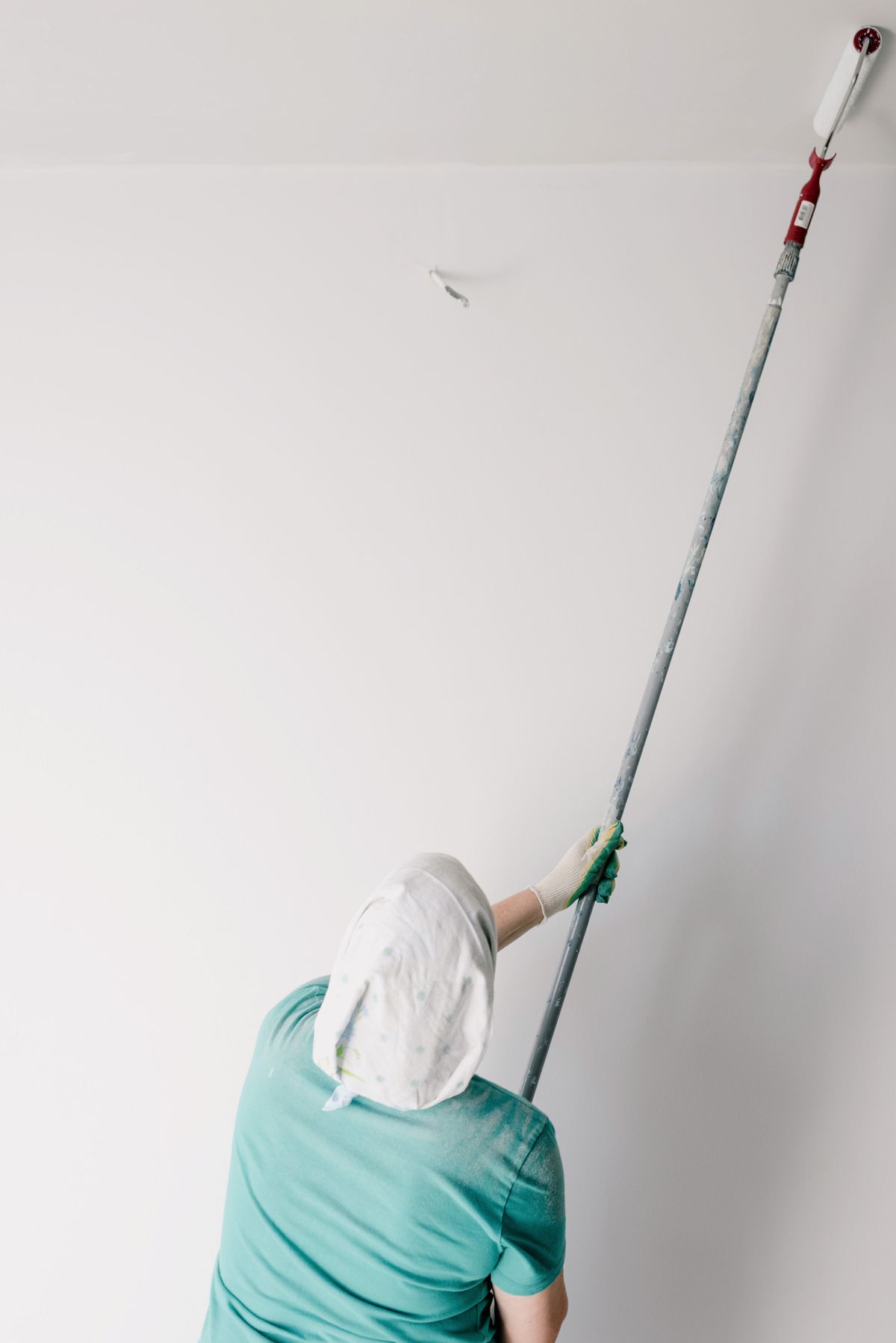 Painter using an extension-pole roller to coat a ceiling in white paint